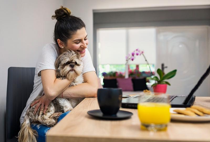 woman using laptop hugs dog